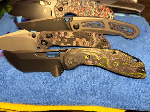 Reviewer's collection of knives, with the Ketuo Yakuza's unique camo carbon handle and open black blade in focus.