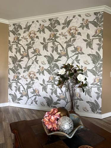 Customer's living room accent wall featuring the lovely Darla Wallpaper with a green and beige floral design.