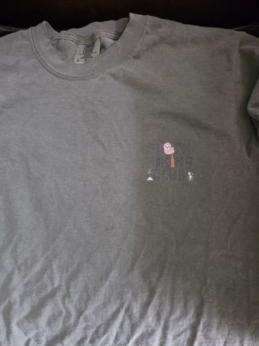 Close-up of a customer's wrinkled green SlothHikingClub T-Shirt showing the faint chest logo.