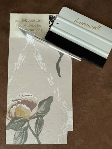 Customer's white application tool, a squeegee, shown with a craft knife and a wallpaper sample.