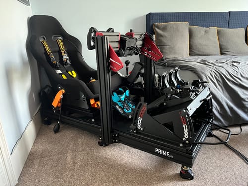 Customer's fully assembled black PRIME Lite Cockpit with a racing seat, wheel, and pedals set up in a room.