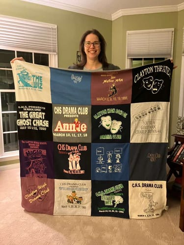 Reviewer proudly holding a large Project Repat T-Shirt Quilt made from old drama club t-shirts.