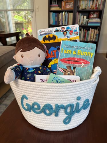 Customer's white woven basket personalized with the name 'Georgie' and filled with books and a doll as a gift.
