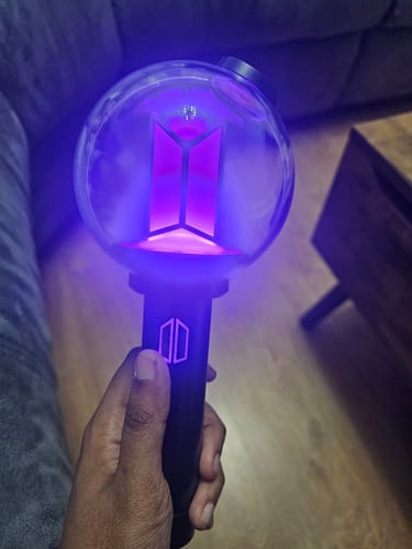 Customer holding the BTS Official Light Stick Ver.4, which is turned on and glowing with a vibrant purple light.