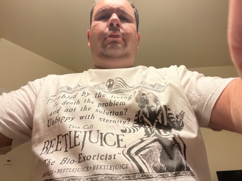 Reviewer in a low-angle shot wearing the white Bio-Exorcist Beetlejuice T-Shirt.