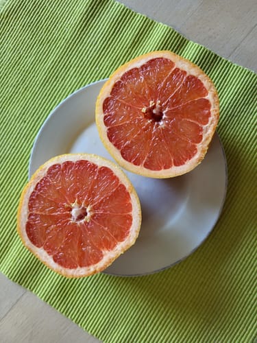Kunde zeigt eine halbierte, rote Grapefruit auf einem Teller, die zum Auslöffeln bereit ist.