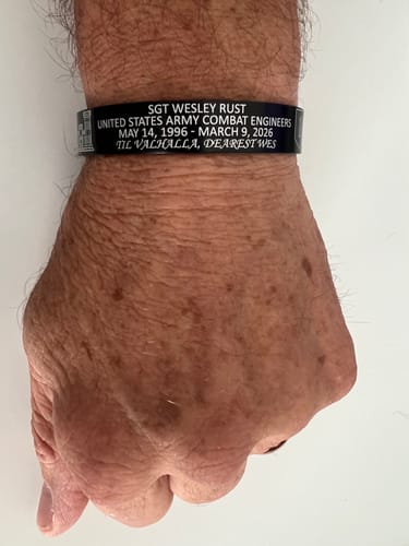 A close-up of a reviewer's wrist wearing a black custom memorial bracelet with four lines of engraved text.