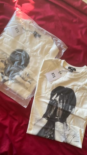 Customer's two BTS - ARIRANG OFFICIAL MD S/S T-SHIRTS laid on a red surface, one unfolded and one in its plastic packaging.
