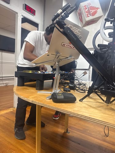 Reviewer, a DJ, using the silver Model-X 2.0 Stand to hold a laptop over a turntable in a studio setting.