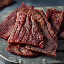Customer's close-up of savory Halal Beef Jerky strips piled together on a dark stone surface.