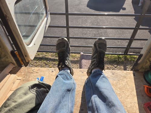Reviewer's first-person view of their worn, dark Active II Pro Barefoot Shoes while sitting outdoors.