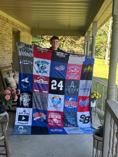 Reviewer's son smiling while holding up a large Project Repat T-Shirt Quilt on a covered porch.