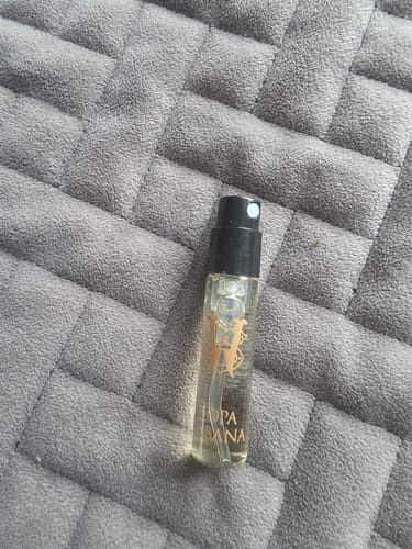 Customer's sample vial of Copacabana fragrance with a black cap, resting on a gray quilted surface.