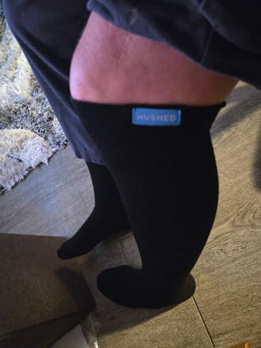 Customer wearing a black knee-high compression sock, showing the snug fit on their leg with the blue brand tab visible.