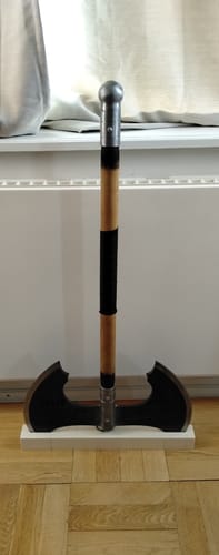 Customer's custom Jotungard axe with double black blades and a wooden handle displayed upright on the floor.