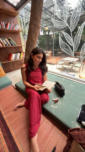 Reviewer sitting in a cafe wearing the maroon flowy linen wide leg pants and matching top.