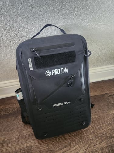 Customer's black FNDN STORM VLT backpack on a floor, with a can shown tightly fitting in the side mesh pocket.