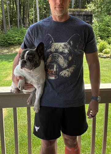 Customer wearing the gray Whiskey Frenchie Grunge T-Shirt while holding a real French bulldog that resembles the graphic.