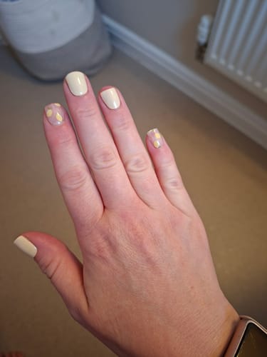 Customer's hand showing a Lemon Drop manicure with pale yellow and dotted accent nails.