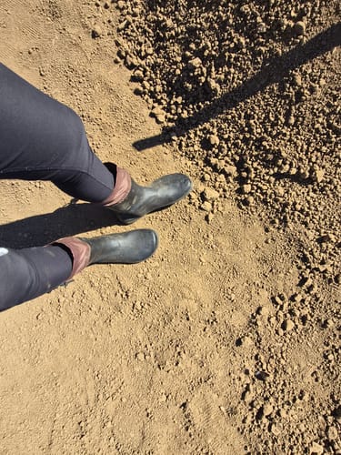 Customer wearing black Brisk Ⅰ - Barefoot Rain Boots while standing on a patch of dry soil.