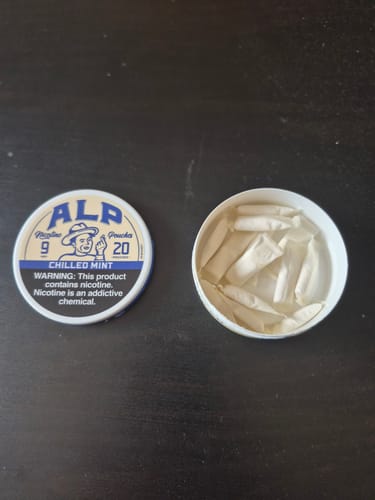 Customer's open can of Chilled Mint Nicotine Pouches with its lid beside it on a dark surface, showing the pouches inside.