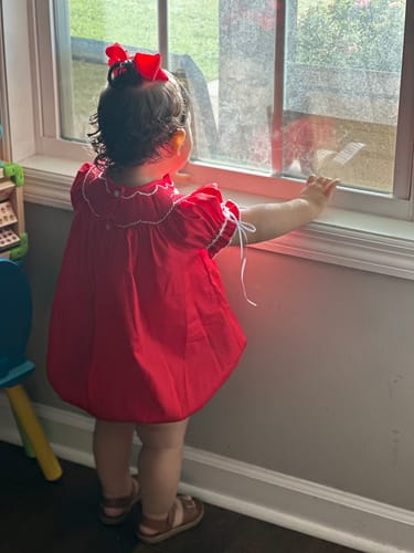 Reviewer's child from behind wearing the red Heart Smocked Pique Bubble while looking out a window.