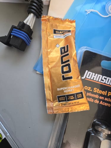 Reviewer's single gold packet of Classic SuperCharged Honey resting on a cluttered work surface.