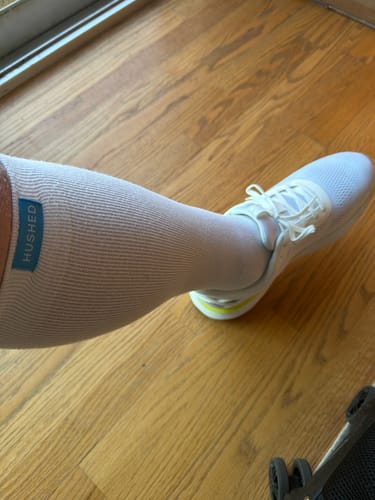 Reviewer wearing a light-colored Eucalyptus Lyocell Compression Sock with a white sneaker on a wood floor.