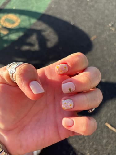 Customer's hand with a Holy Gels manicure, showing short, pale pink nails with daisy and gold leaf accent designs.