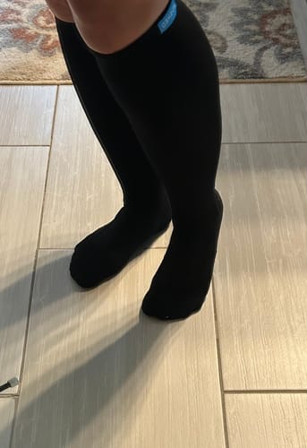 Customer wearing the black Eucalyptus Lyocell Compression Socks, showing the fit from knee to foot on a tiled floor.