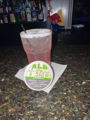 Customer's can of Spearmint Nicotine Pouches on a bar counter next to a pink cocktail.