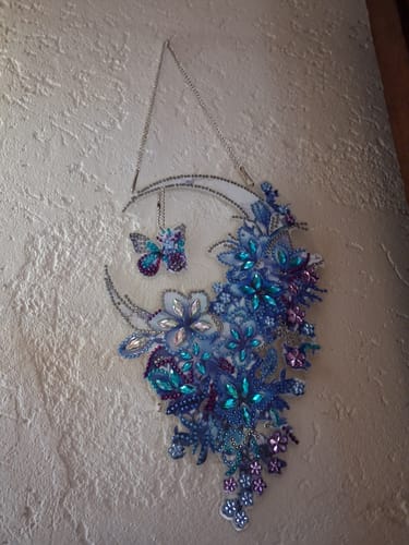 Recensent toont de voltooide Diamond Painting Dromenvanger, met blauwe bloemen en een vlinder, hangend aan een muur.