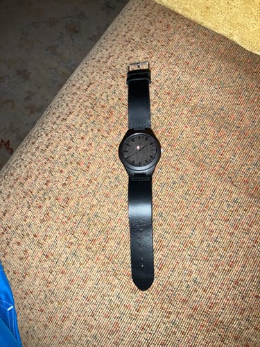 A customer's black Premium Engraved Wood Watch with a leather band laid out on a textured fabric surface.