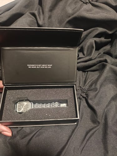 Reviewer holding the open black box of the CLAIRE DE MAINS watch, showing the silver timepiece inside.