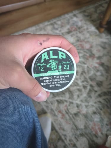 Reviewer holding a round, green and black tin of ALP Refreshing Chill Nicotine Pouches.
