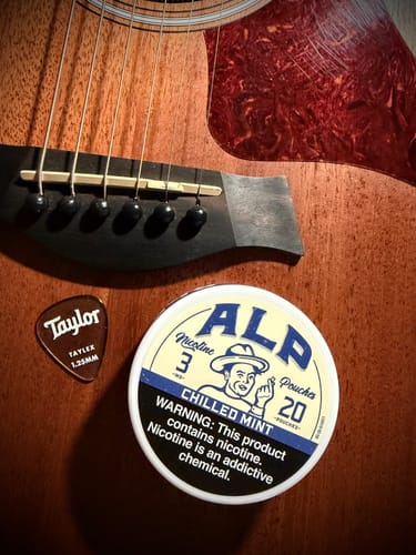 Customer's can of ALP Chilled Mint Nicotine Pouches sitting on a wooden acoustic guitar next to a pick.