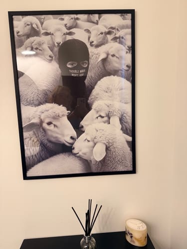 Customer's 'Built Different' art print hanging on a wall in a black frame, depicting a masked figure among sheep.