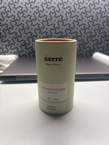 Customer's off-white, cylindrical packaging for their new Midnight Whisper perfume on a desk.