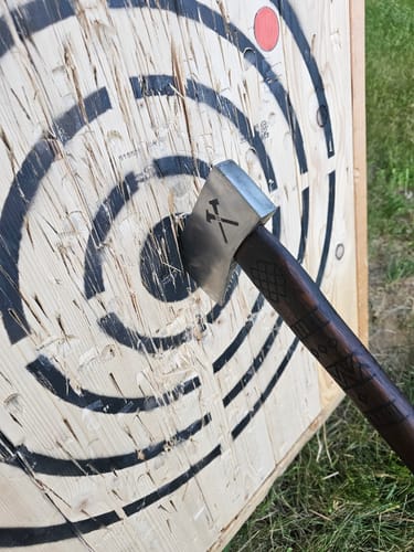 Customer's 'Vargr' throwing axe with a carved handle embedded in a wooden practice target.