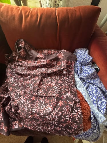 Customer's surprise printed cotton fabric with a dark brown and pink floral design, piled on a chair.