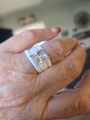Customer wearing two white Stackable Thin Silicone Wedding Rings framing a solitaire diamond ring on their finger.