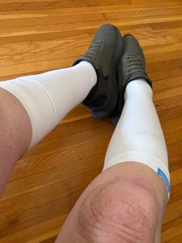 Reviewer wearing white Eucalyptus Lyocell Compression Socks pulled up to their knees while sitting.