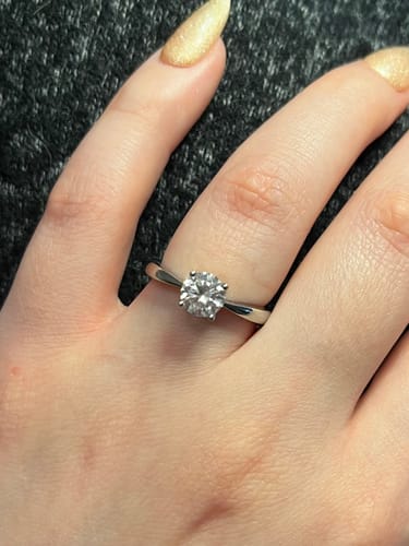 Customer's hand showing the shiny Simple Round Solitaire Ring with a sparkling stone.