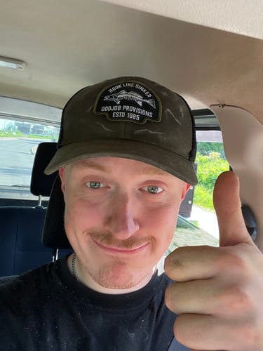 Customer wearing a green Big Logger Hat, smiling and giving a thumbs-up.