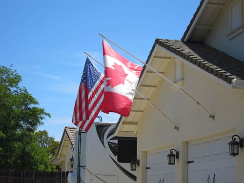 Customer's Canadian Flag flying on a flagpole from the side of a house on a sunny day.