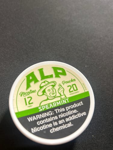Customer's tin of ALP Spearmint Nicotine Pouches with 12mg strength shown on a dark surface.
