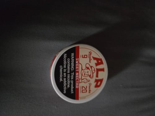Reviewer's can of ALP Sweet Nectar Nicotine Pouches shown on a dark surface.