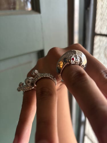 Customer's hand wearing two ornate, silver-colored rings, showing off the detailed designs.