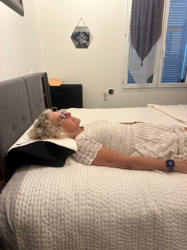 Personne allongée sur le dos utilisant l'oreiller Papillon Cervical Cellsius dans un lit.