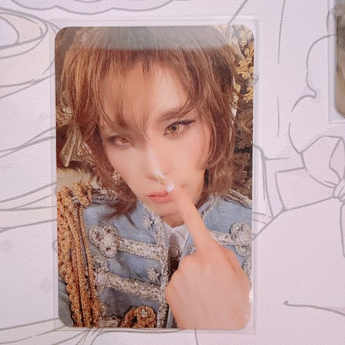 Customer's XLOV 'I,God' official photocard of a person in a blue ornate jacket touching their nose with their finger.